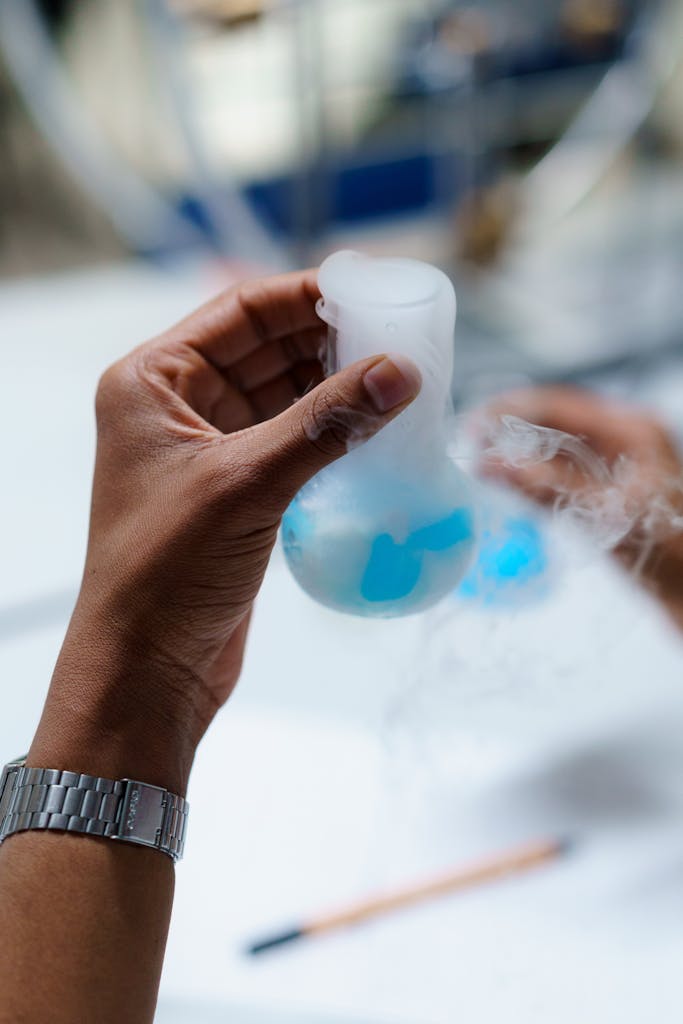 Close-up of scientist's hand holding a flask with vapor in a laboratory setting.
